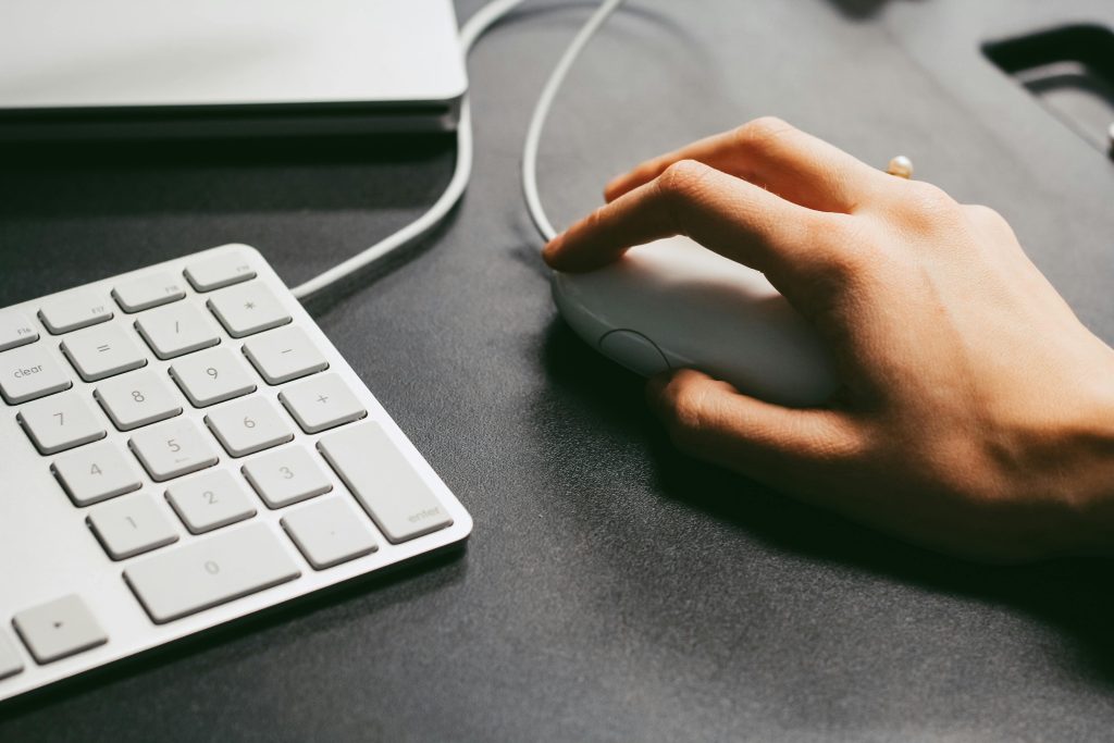 Hand operates a computer mouse beside a white keyboard on a dark desk, showcasing modern technology use.